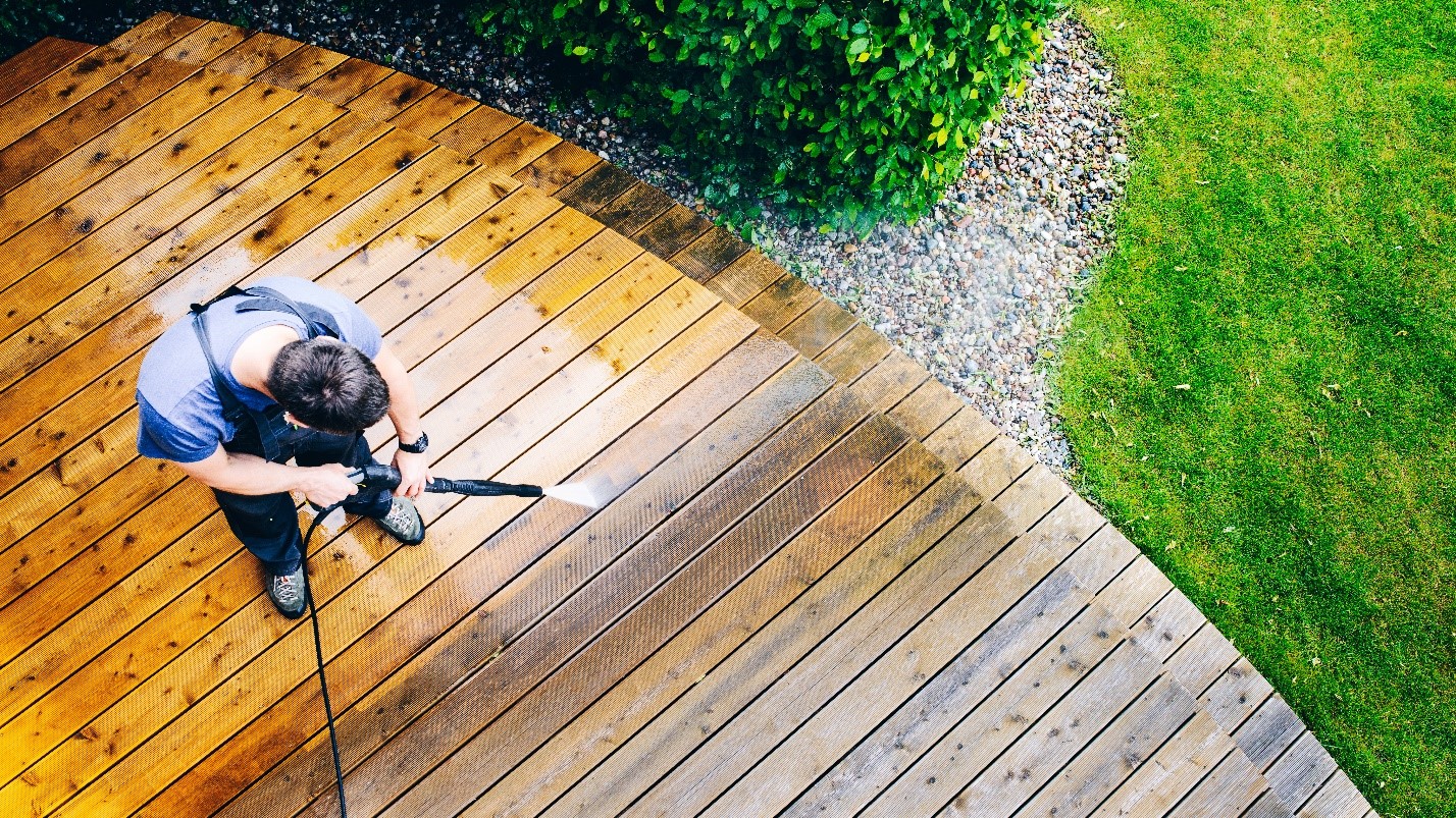 A homeowner with a power washer cleans their outdoor deck 